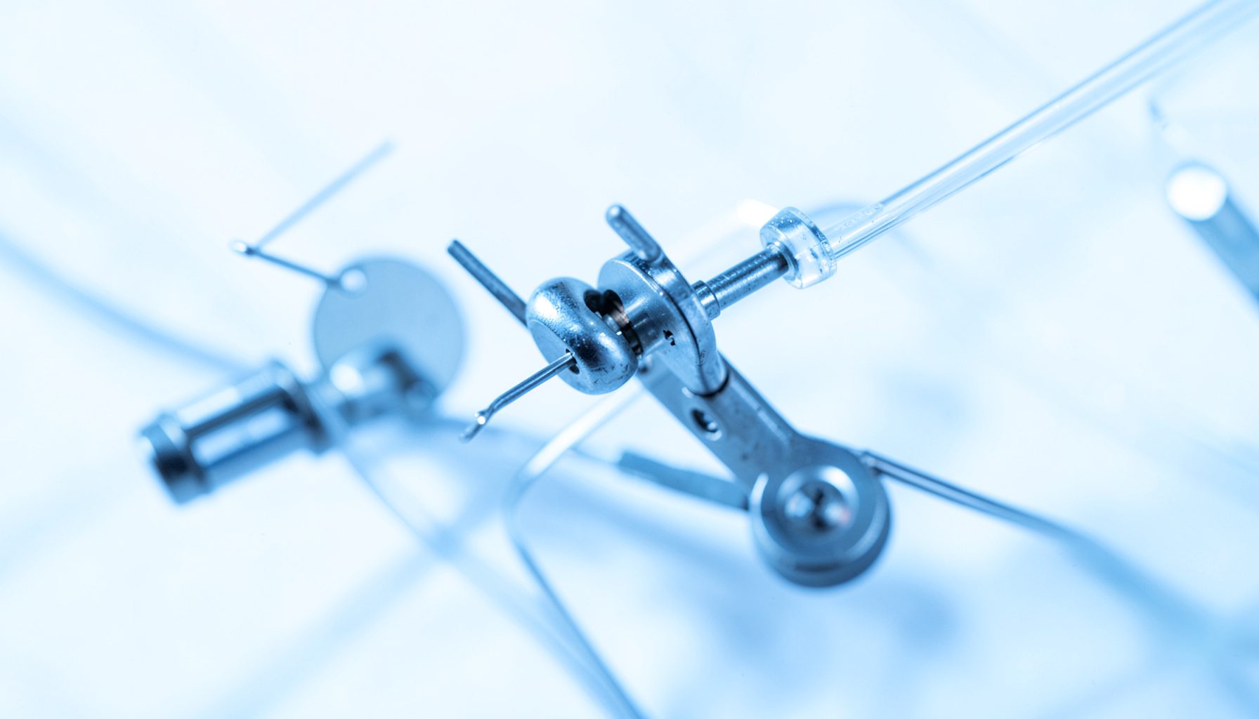 A close-up of precision laboratory equipment with metallic sensor components and fine tubing, illuminated by cool blue-toned light against a clean white background, conveying scientific rigor and industrial measurement.